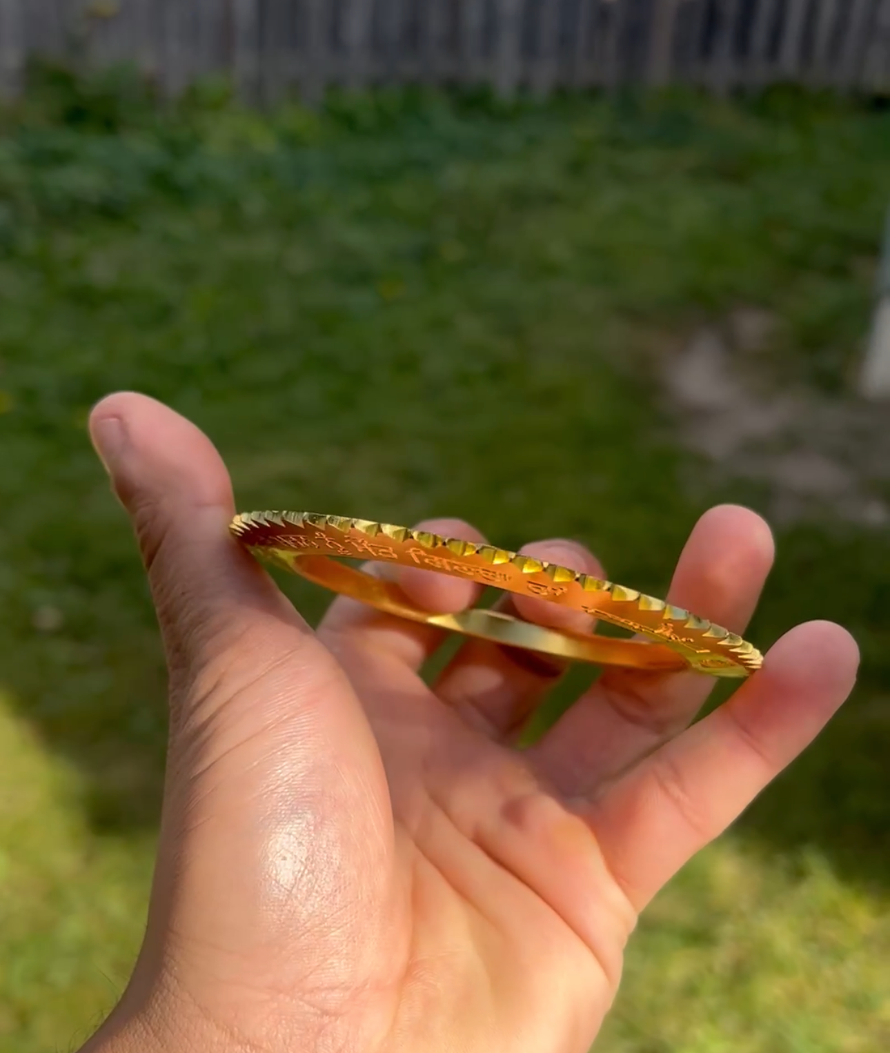 Hand holding a gold bracelet with a grassy background